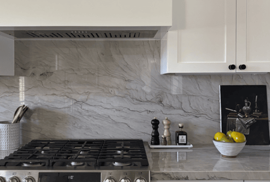 Modern kitchen featuring marble backsplash with gray veining, white cabinetry, and a stainless steel gas stove. The scene is