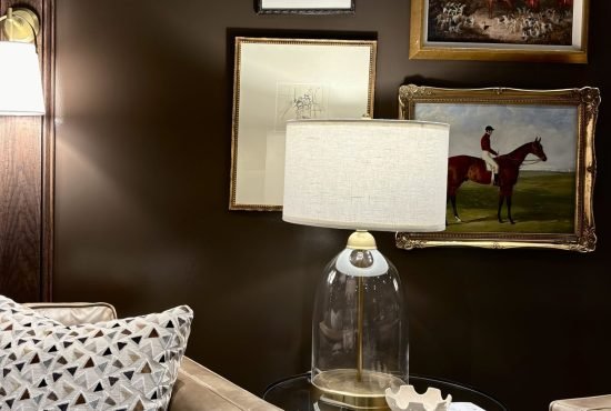 Cozy living room corner featuring a vintage glass lamp, framed artwork, and a neutral-toned sofa, with dark brown walls that