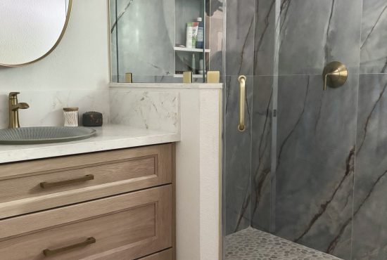 Modern bathroom with a glass shower enclosure featuring marble-like walls, a pebble stone floor, and wooden cabinetry.