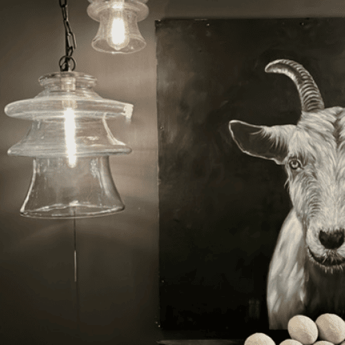 Modern interior featuring a dark wall with a prominent goat portrait and hanging glass pendant lights. The mood is contempora