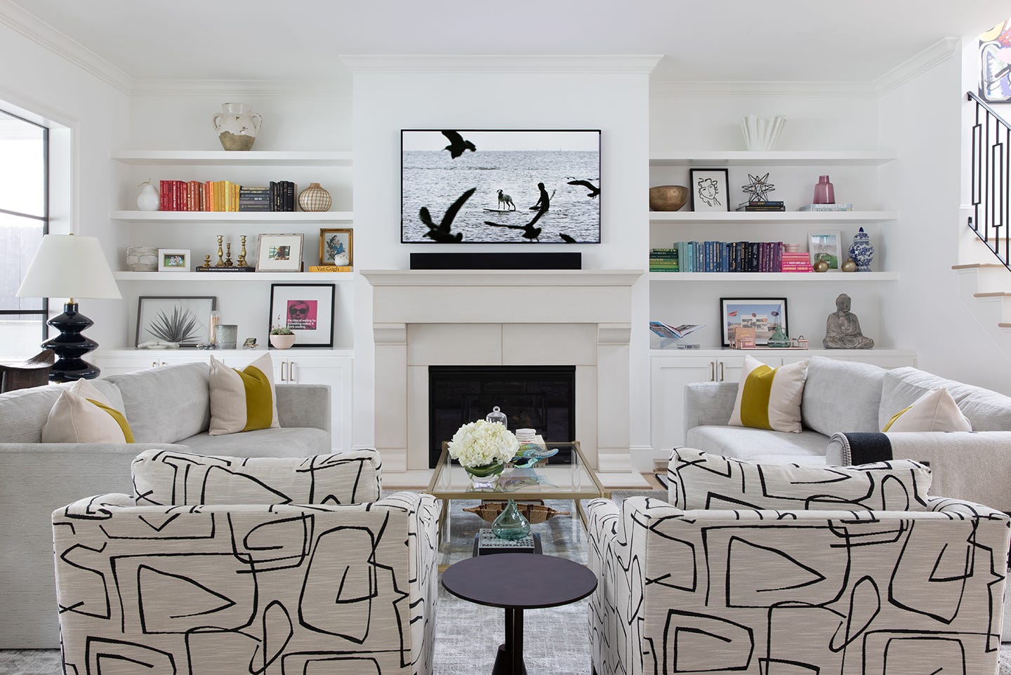 Modern living room with neutral-colored sofas and patterned chairs, featuring built-in shelves adorned with books and decorat