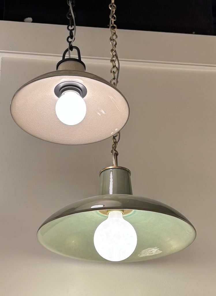 Two hanging pendant lights with a minimalist design; the upper light features a white bulb and a plain shade, while the lower