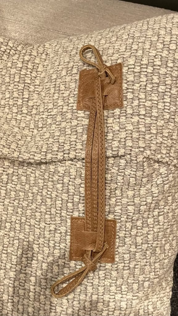 Close-up of a textured, woven fabric cushion with a brown leather strap attached, indicating a casual and cozy interior style