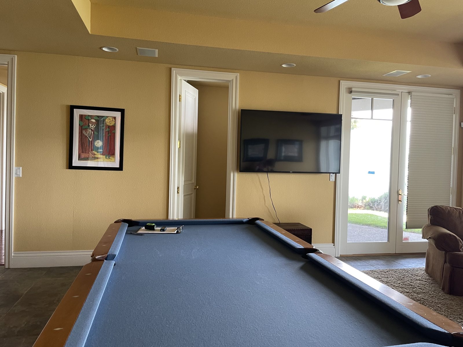 A game room with a pool table, wall-mounted TV, framed artwork, and glass doors leading outside. — Interior Design in Elk Grove, CA 95624