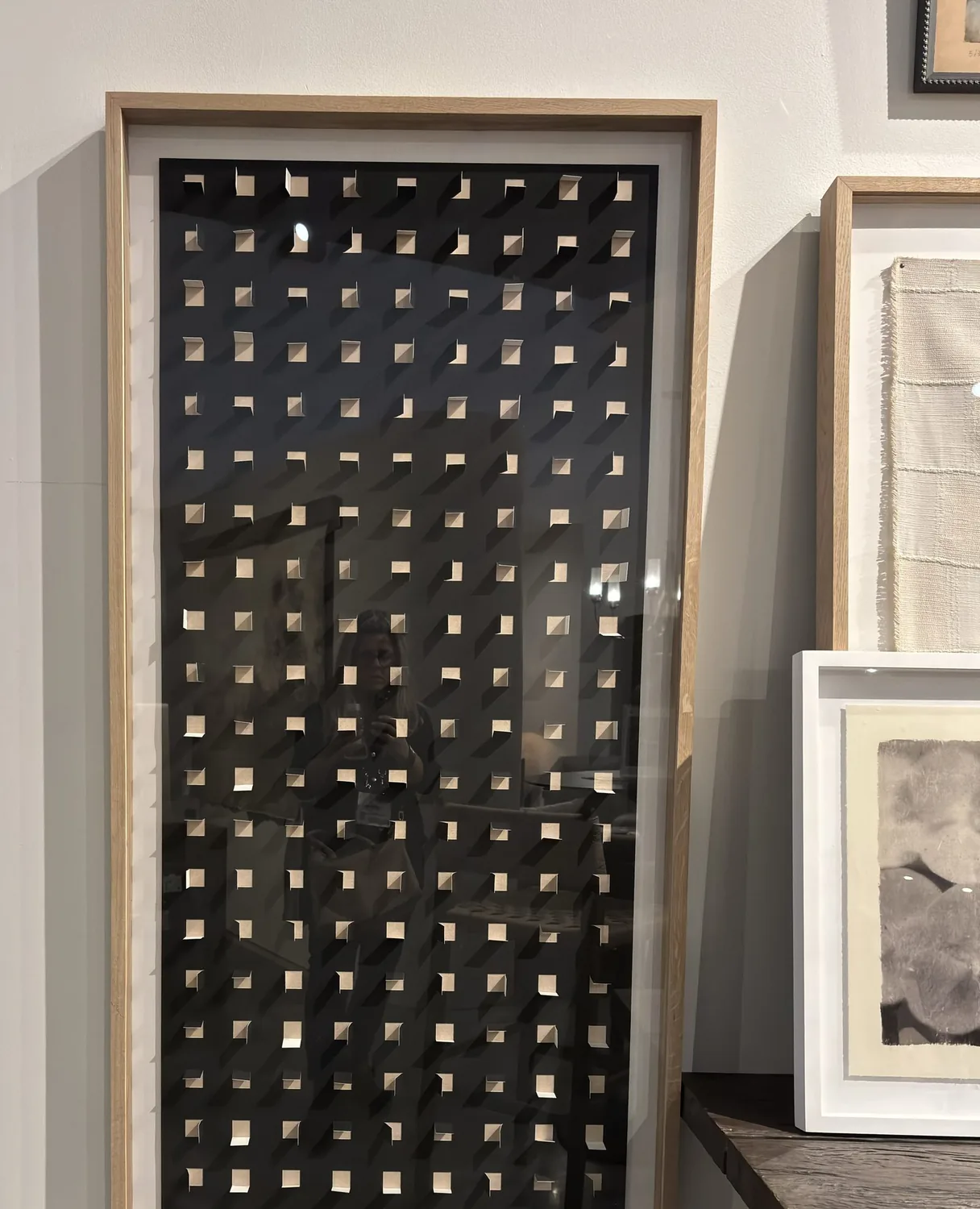 A framed piece of modern art with a grid of small square cutouts casting shadows on a black background, displayed