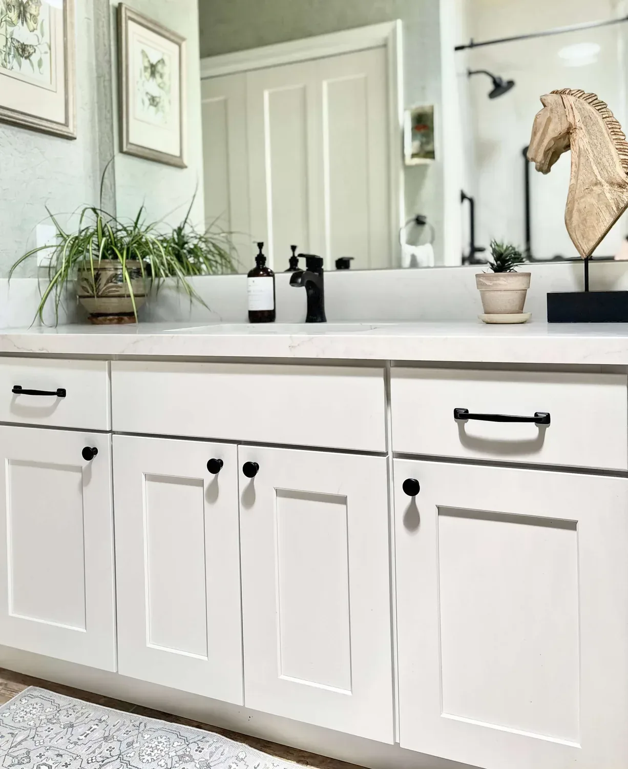 A modern bathroom with dark stone tiles, a double sink vanity with wood cabinetry, a large backlit mirror, a glass