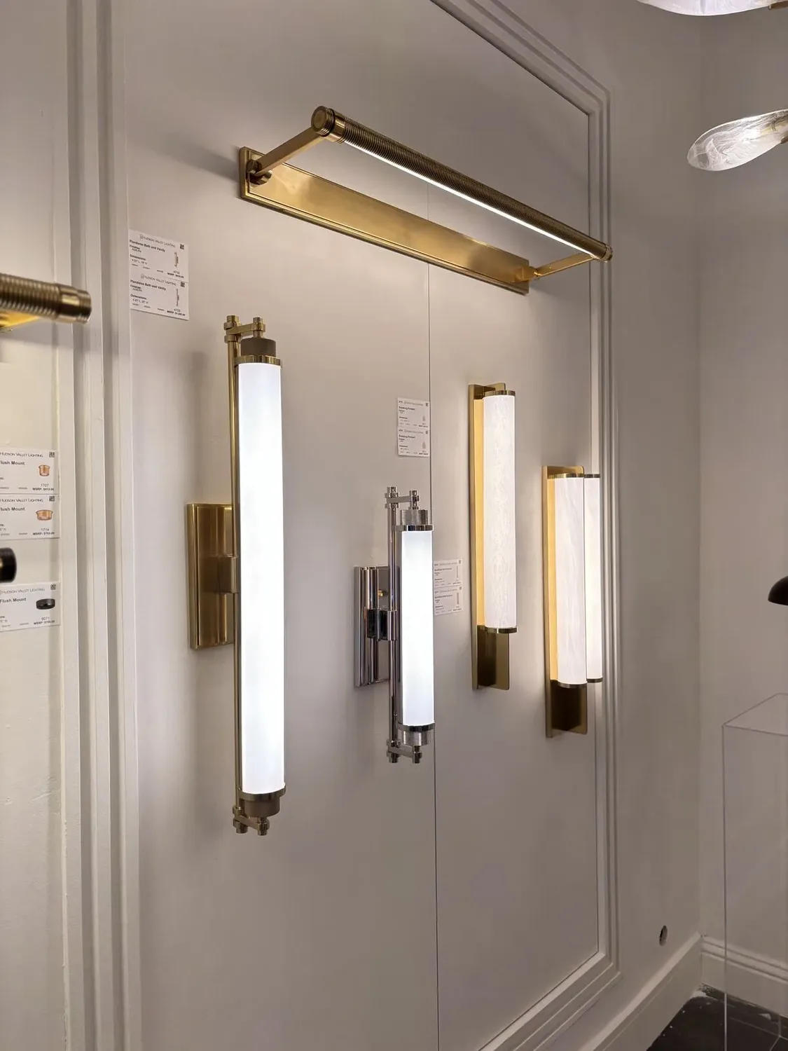 A display of modern wall-mounted light fixtures in brass and chrome finishes on a white paneled wall