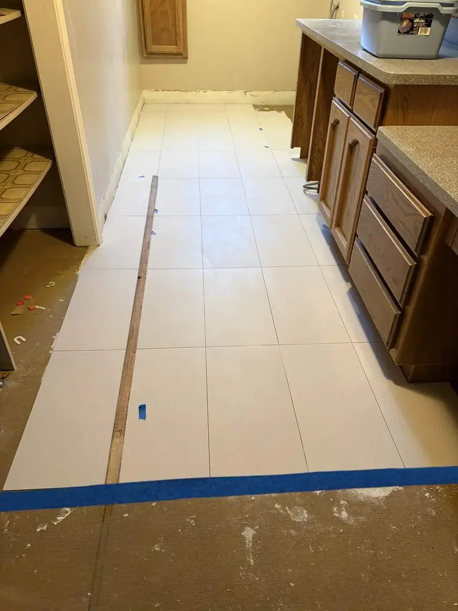 A kitchen floor renovation in progress with newly installed large white tiles and wooden cabinets