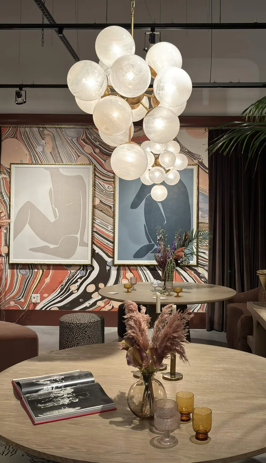 A dining room with a wooden table, cowhide upholstered chairs, a floral centerpiece, large windows with beige curtains