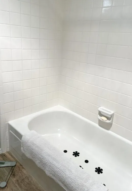 A white bathtub with a towel draped over the edge, surrounded by white tiled walls and a soap holder with a bar of soap