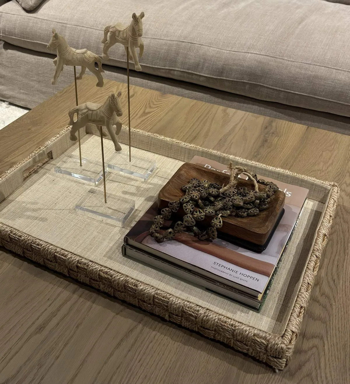 A close-up of a woven tray on a wooden coffee table holding decorative horse figurines, a wooden bowl with beads