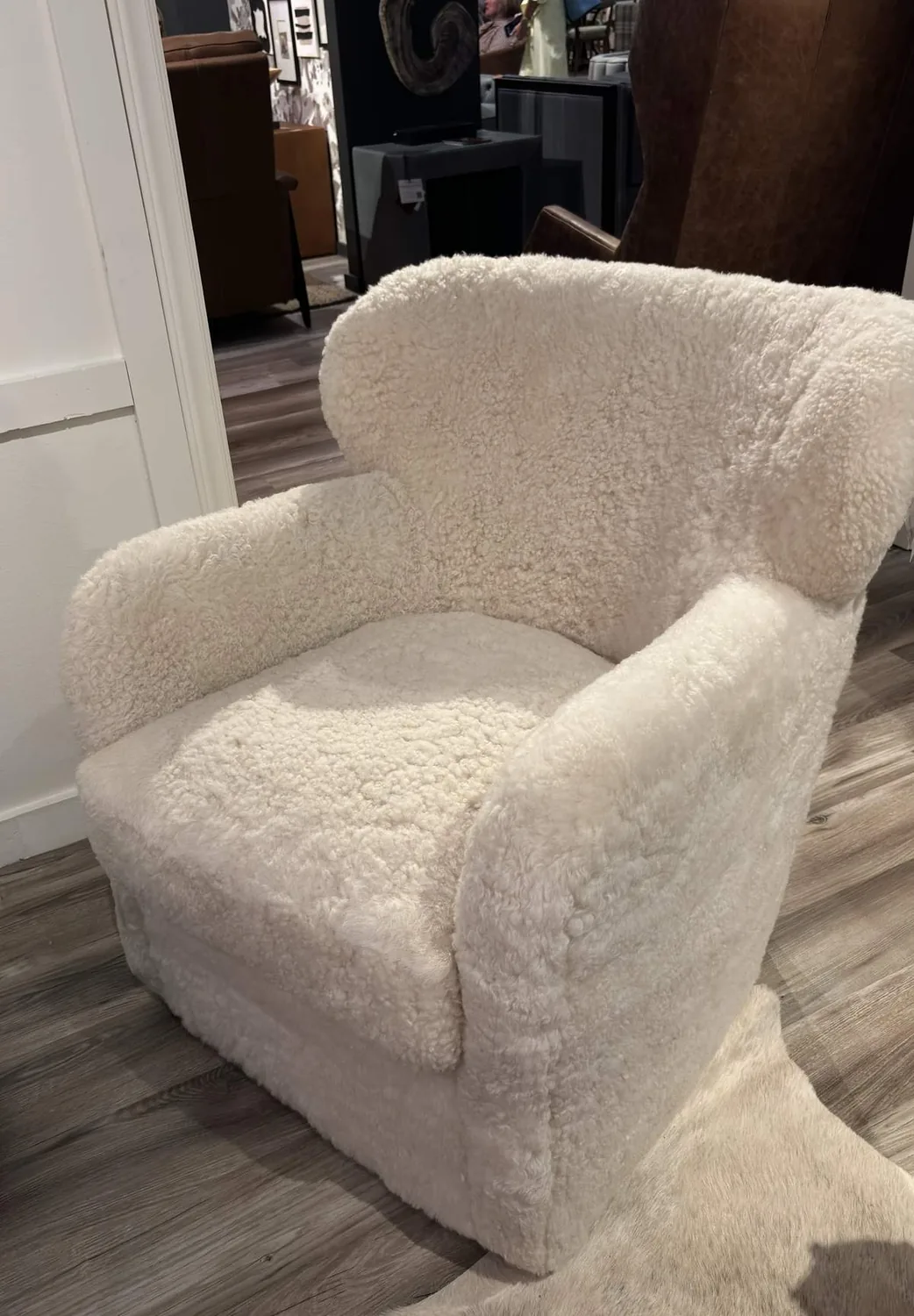 A cozy, plush armchair upholstered in white sherpa fabric placed on a wooden floor next to a white wall