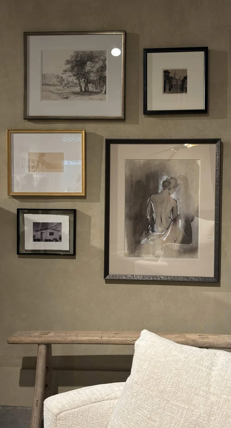 A wall with five framed artworks above a wooden bench and a white textured cushion