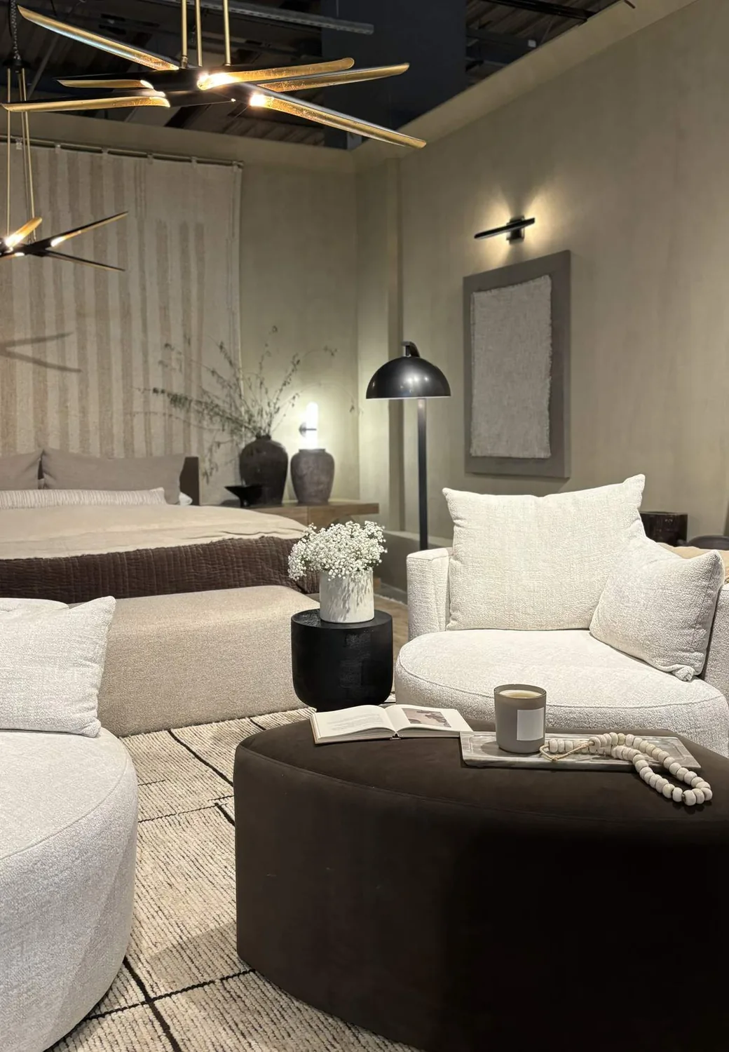 A modern bedroom and living area with neutral tones, featuring a round white armchair, a bed with brown bedding, contemporary lighting fixtures, and minimalist decor