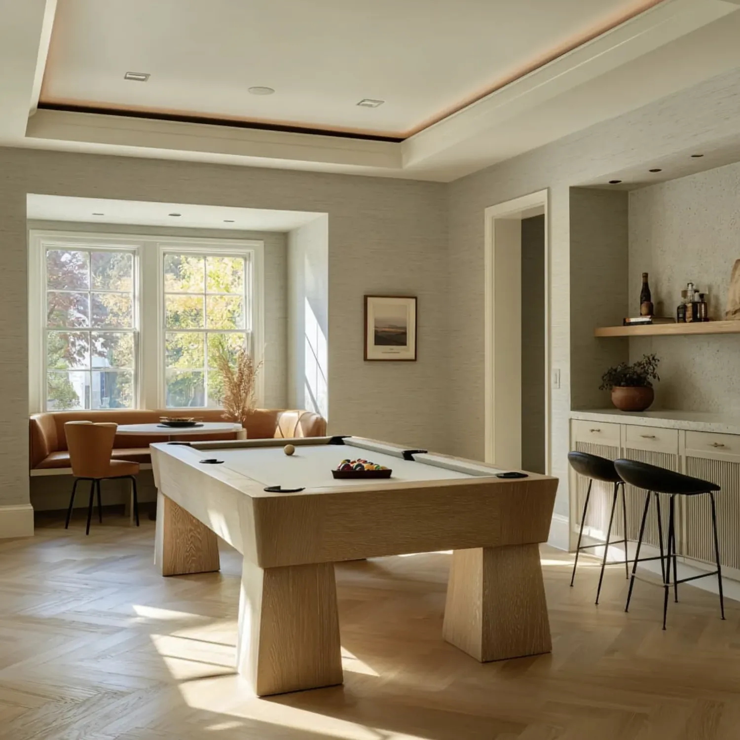 A bright, modern game room with a pool table, built-in seating by large windows, and a bar area with stools