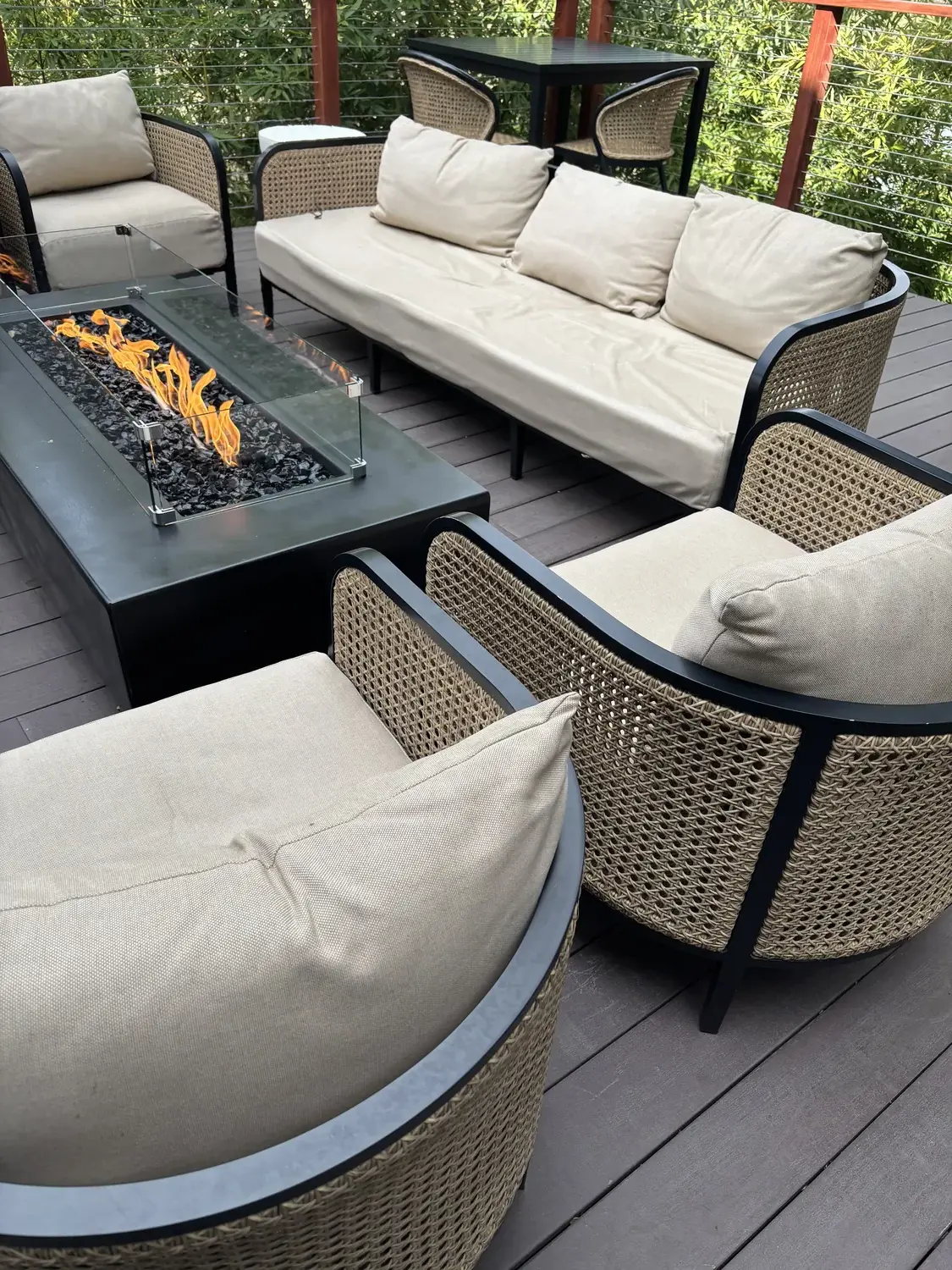 Outdoor seating area with beige cushioned wicker chairs and a fire pit table on a wooden deck