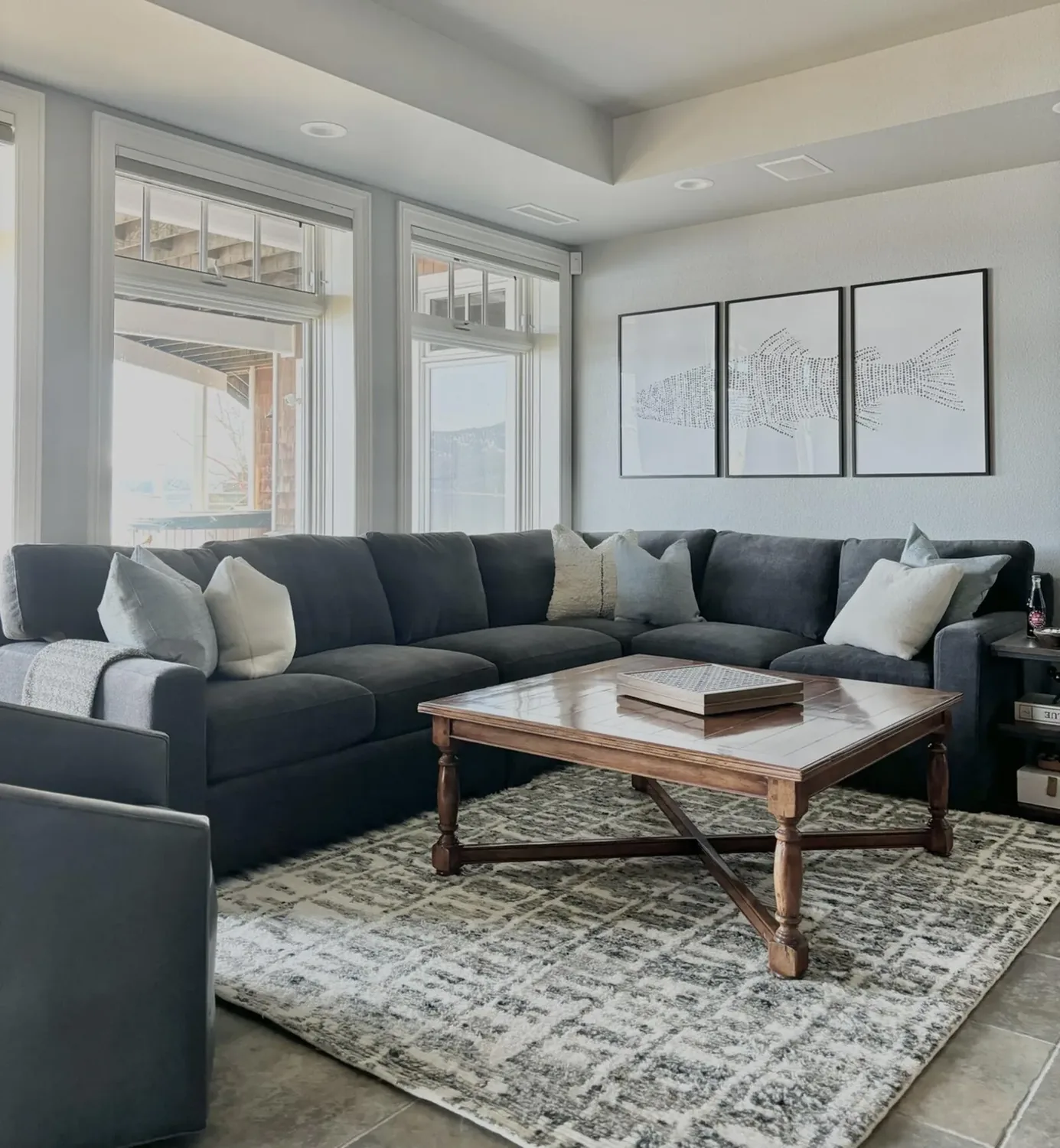 A modern living room corner with a beige sofa, decorative pillows, a wooden sideboard with wine bottles and glasses