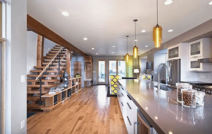 A modern open-concept kitchen and living area with wooden floors, a staircase with wooden steps