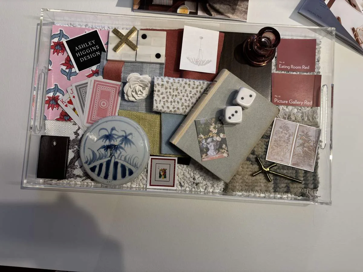 A clear tray containing various design samples including fabric swatches, paint chips, playing cards, dice, a small ceramic plate, and decorative items