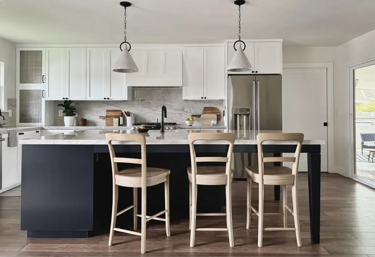 A modern kitchen with white upper cabinets, a black island with a white countertop, three wooden bar stools