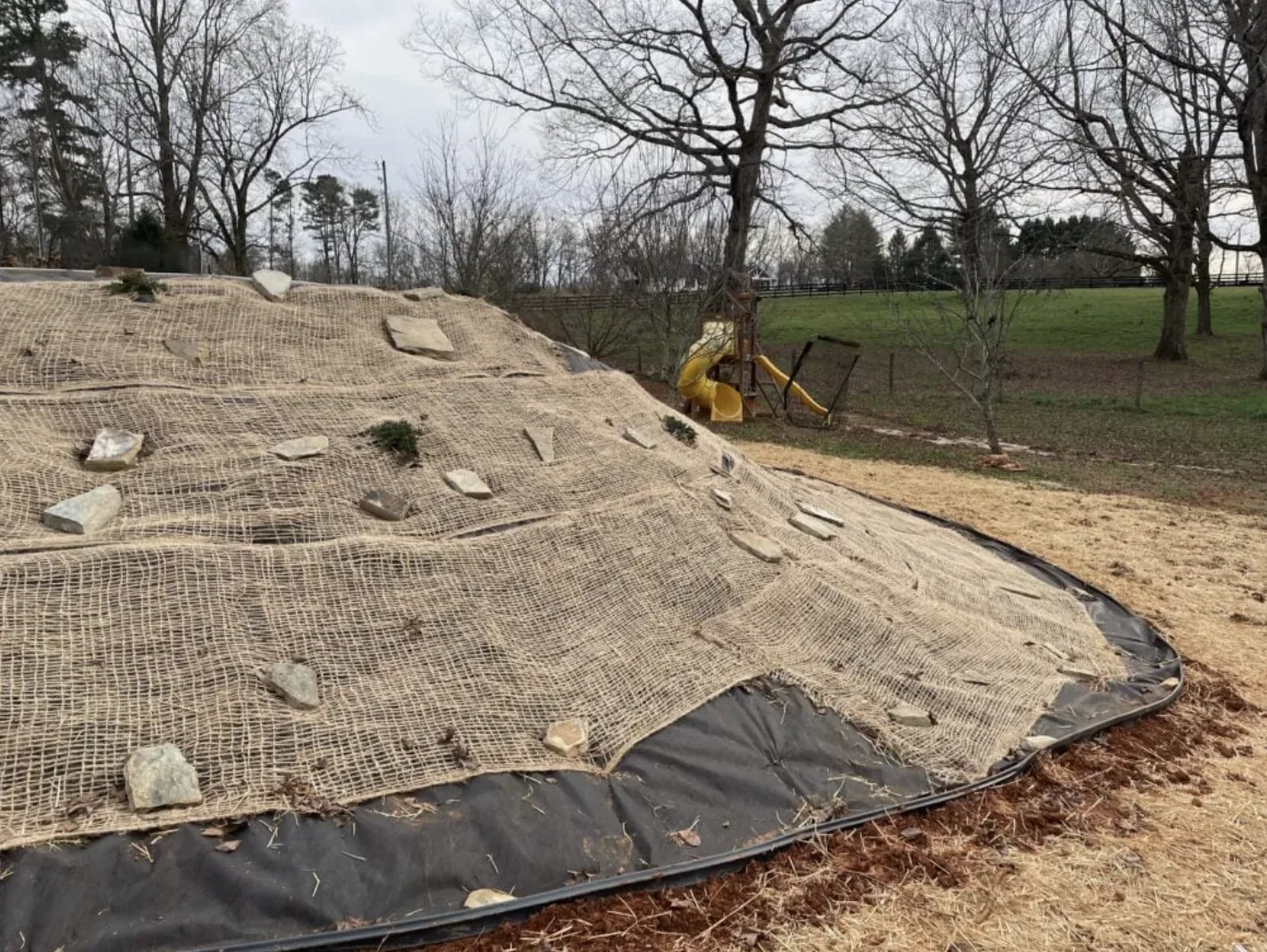 A sloped outdoor area covered with erosion control netting and rocks, with a playground slide