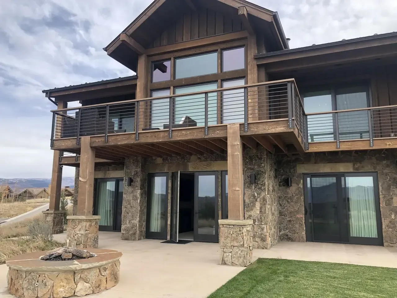Exterior view of a two-story house with stone and wood construction, featuring a balcony with metal railing and a stone