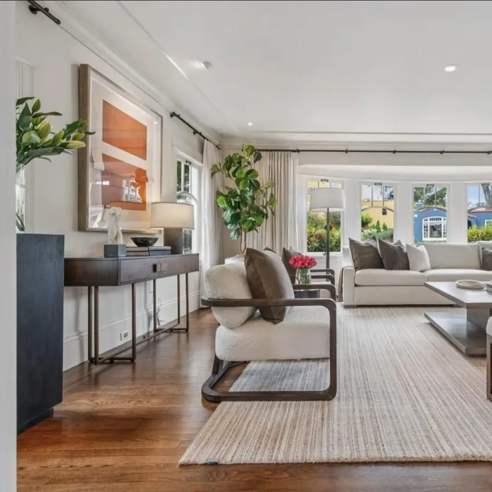 A bright and modern living room with large windows, neutral furniture, and wooden flooring