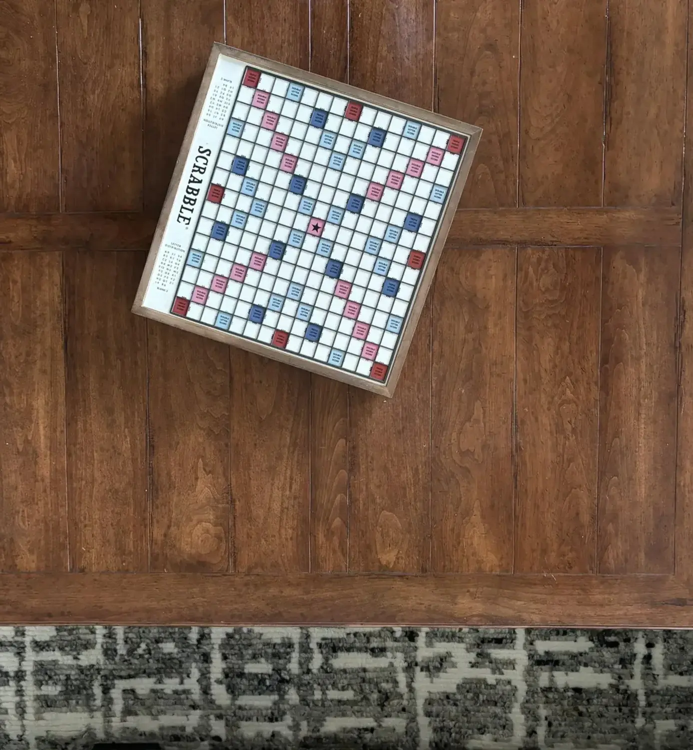 A Scrabble board on a wooden table next to a patterned rug