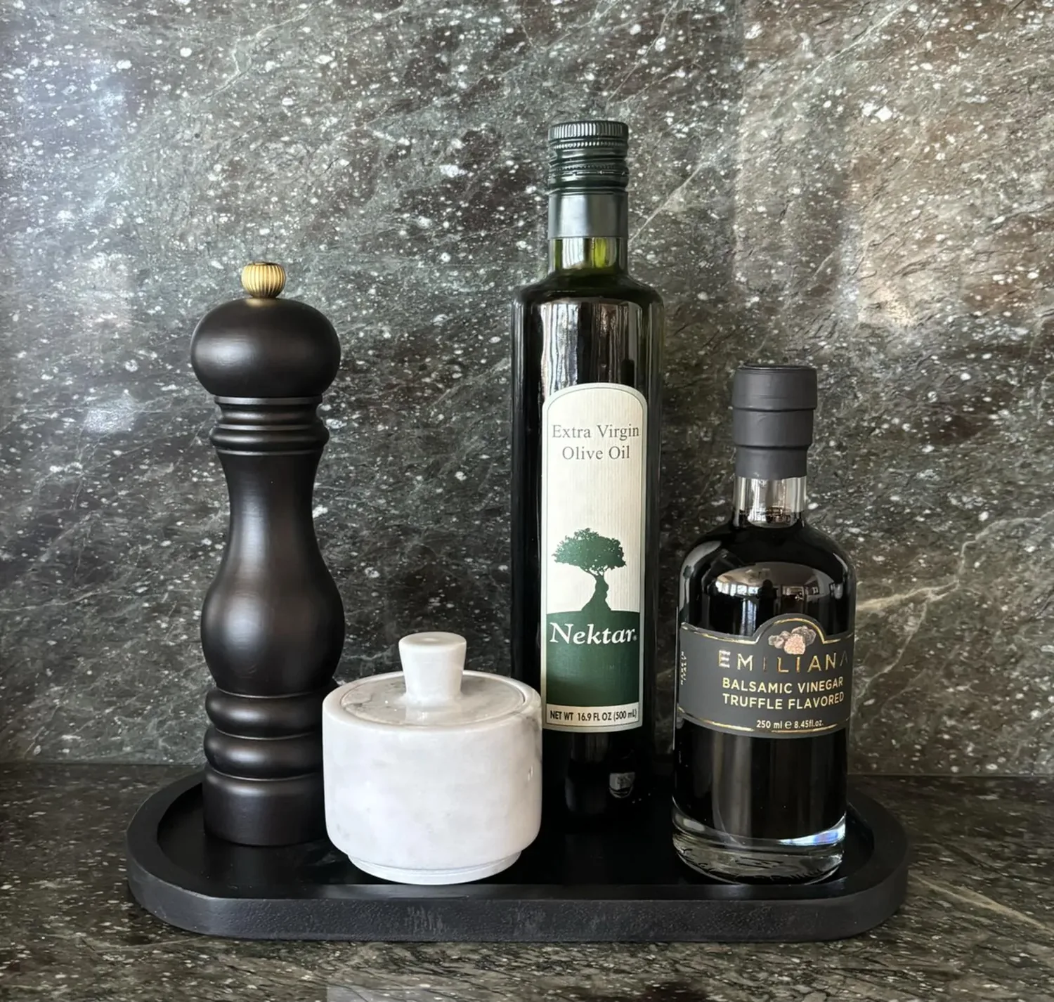 A kitchen countertop display featuring a pepper grinder, a marble container, a bottle of extra virgin olive oil