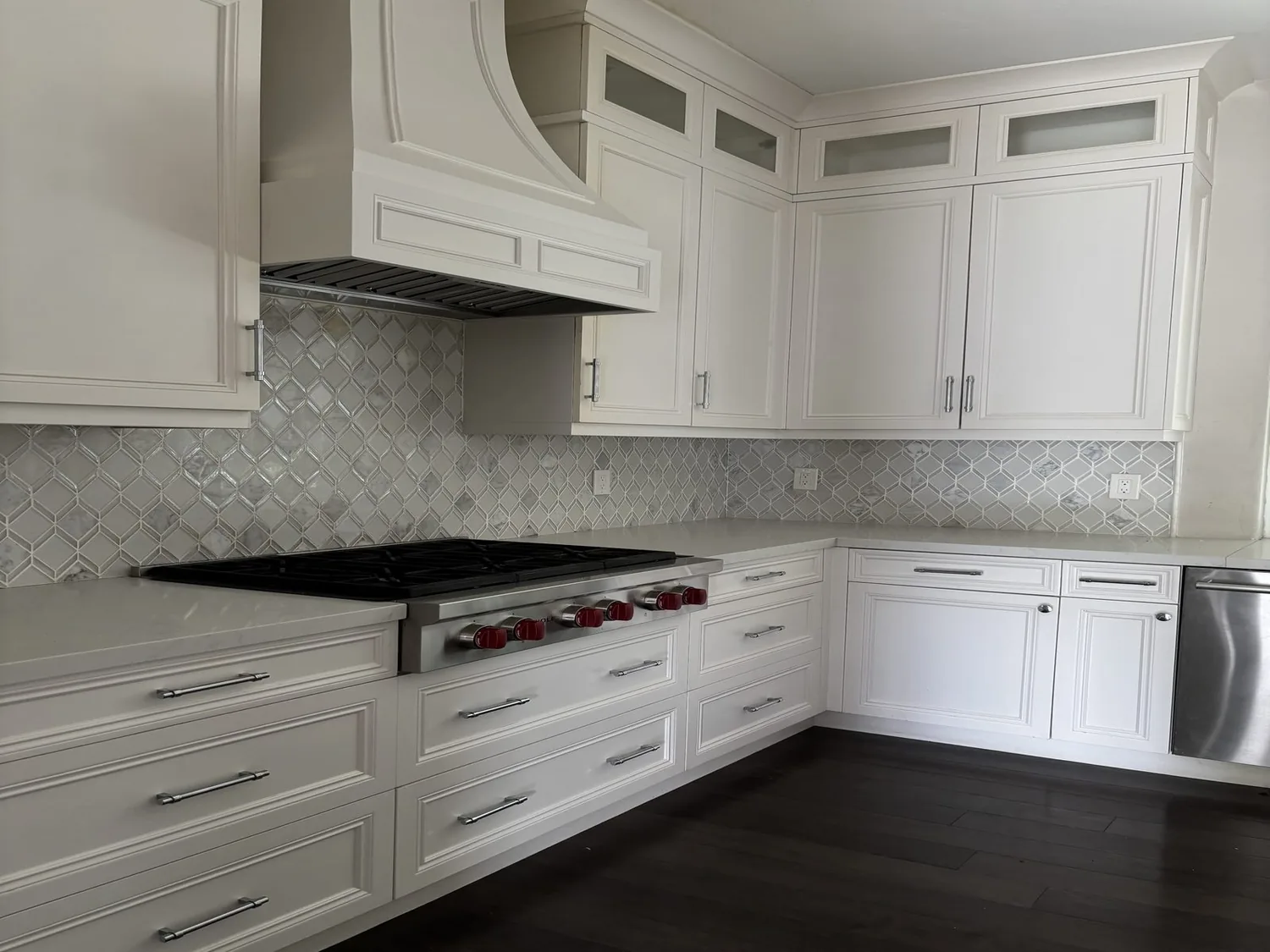 A modern white kitchen with a stainless steel stove, white cabinetry, and a patterned tile backsplash