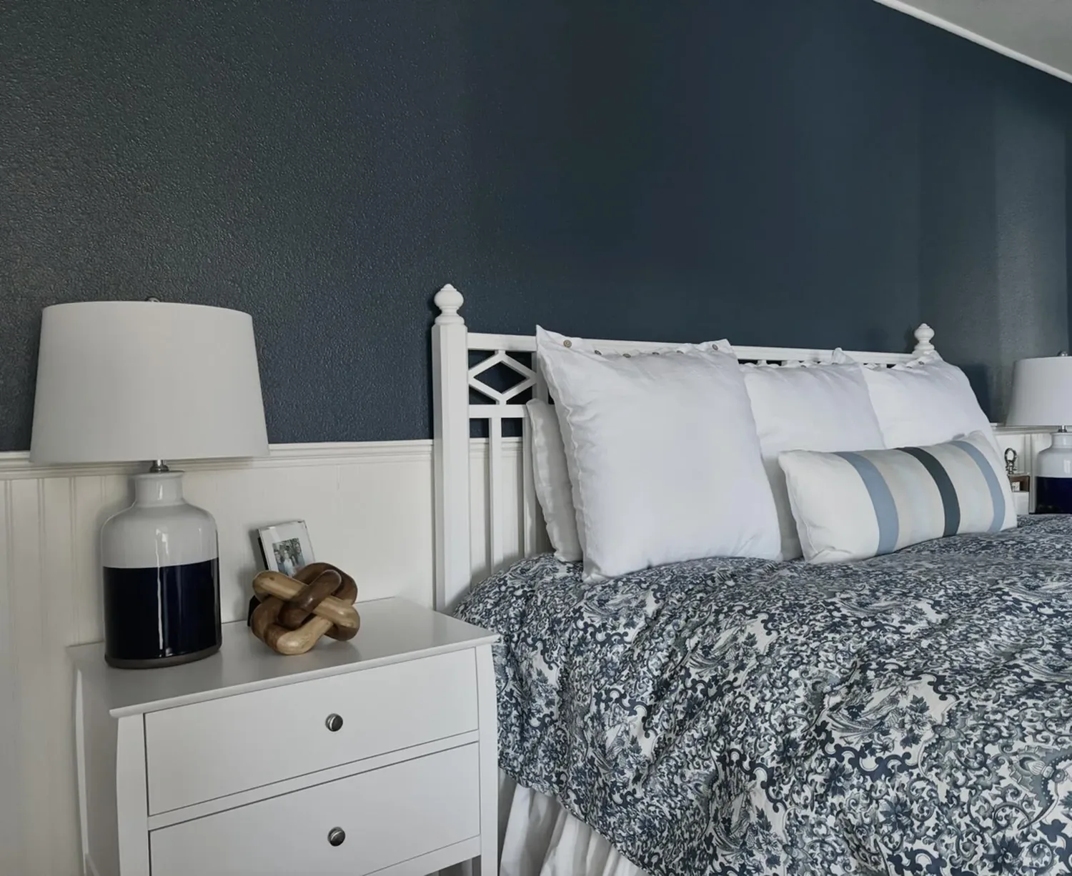 A bedroom with a white bed frame, blue patterned bedding, white pillows, and matching bedside tables with lamps