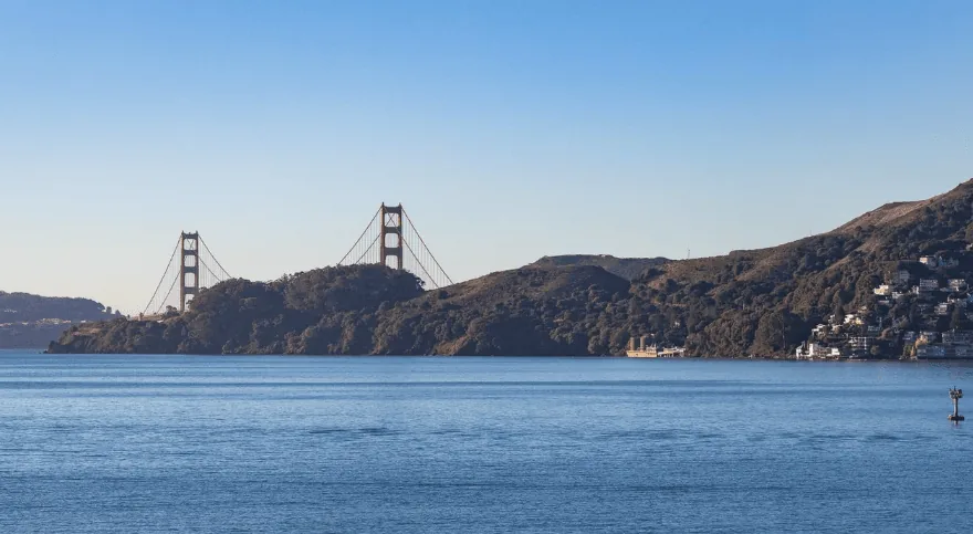 View of the Golden Gate Bridge and surrounding hills across a body of water under a clear sky