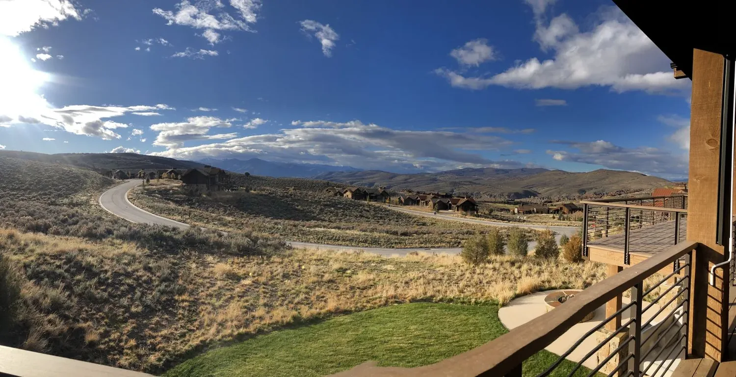View from a balcony overlooking a winding road, dry grassy hills, and distant mountains under a partly cloudy sky