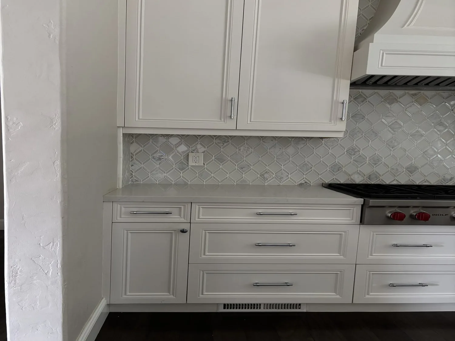 A modern kitchen section featuring white cabinetry, a marble-patterned tile backsplash
