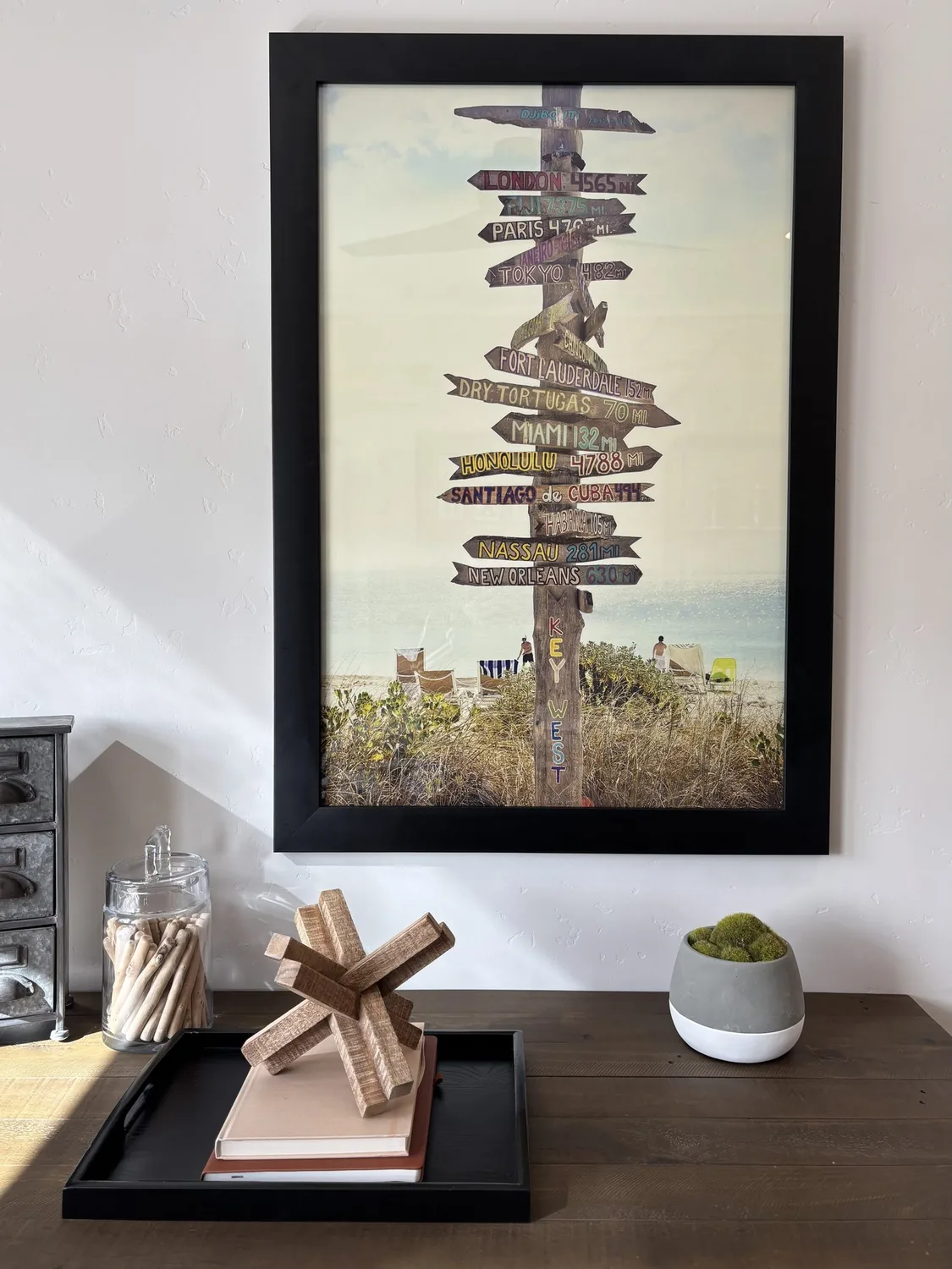 A framed photo of a wooden signpost with multiple directional signs showing distances to various cities, set against
