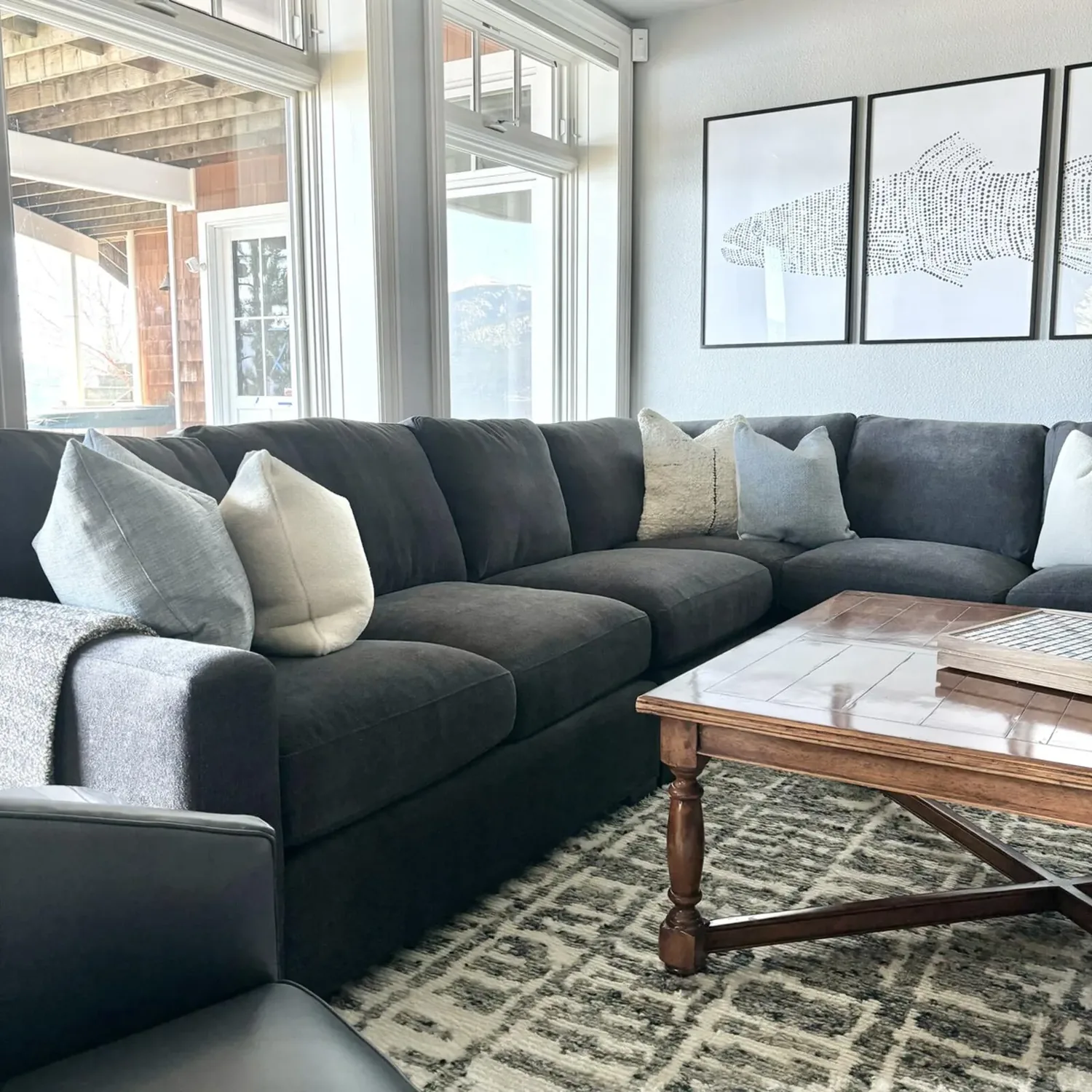 A modern living room with a dark gray sectional sofa, light-colored pillows, a wooden coffee table, and three framed