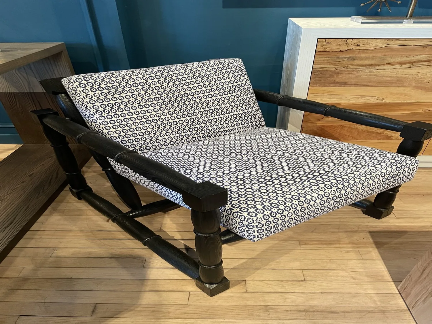 A patterned cushioned chair with dark wooden frame set on a light wood floor against a blue wall