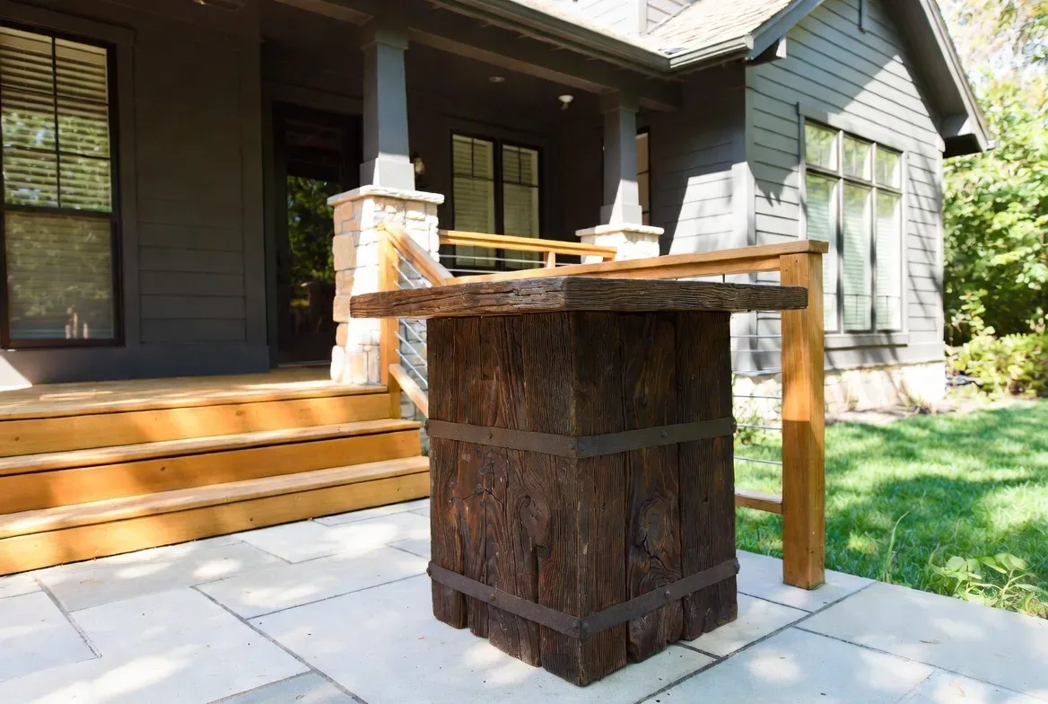 Outdoor patio area with a rustic wooden table and steps leading to a house with gray siding