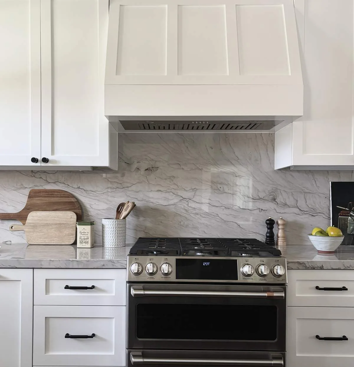 A modern kitchen featuring white cabinetry, a stainless steel stove, and a marble backsplash and countertop