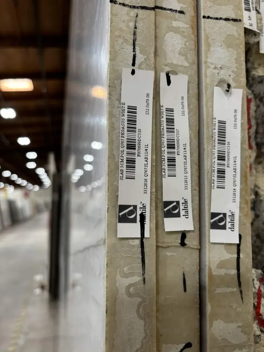 Close-up image of stacked slabs of Pegasus White polished stone with DalTile labels in a warehouse