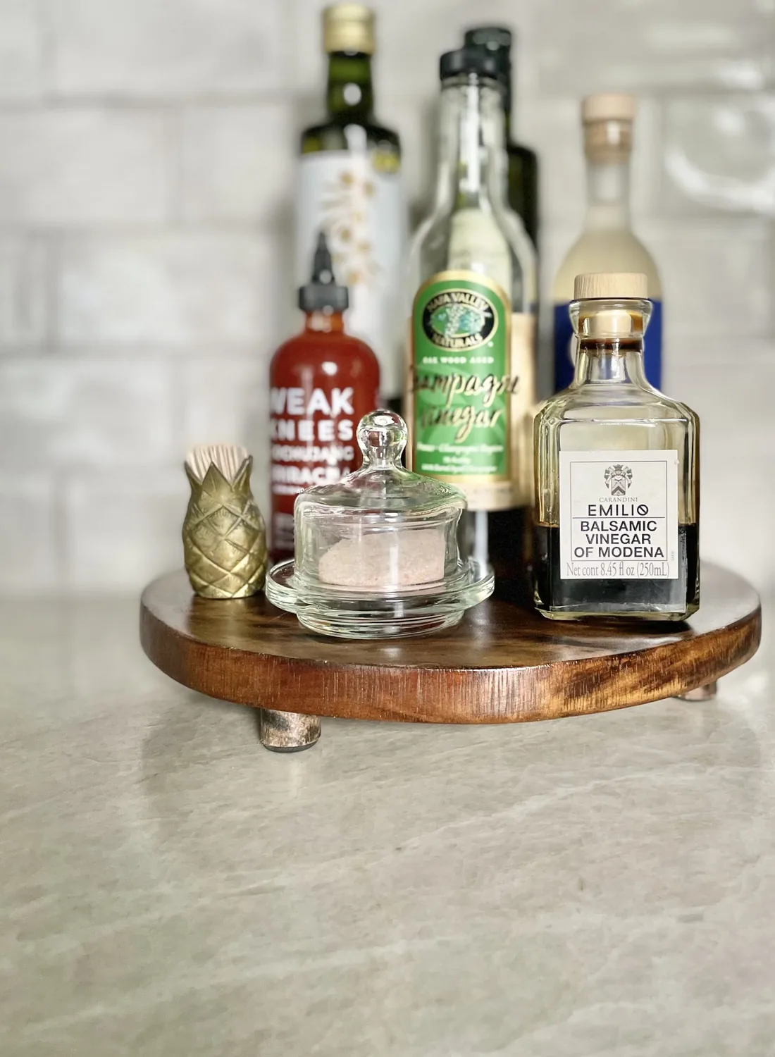 A wooden lazy susan on a kitchen countertop holding various condiment bottles and a small glass container with pink salt