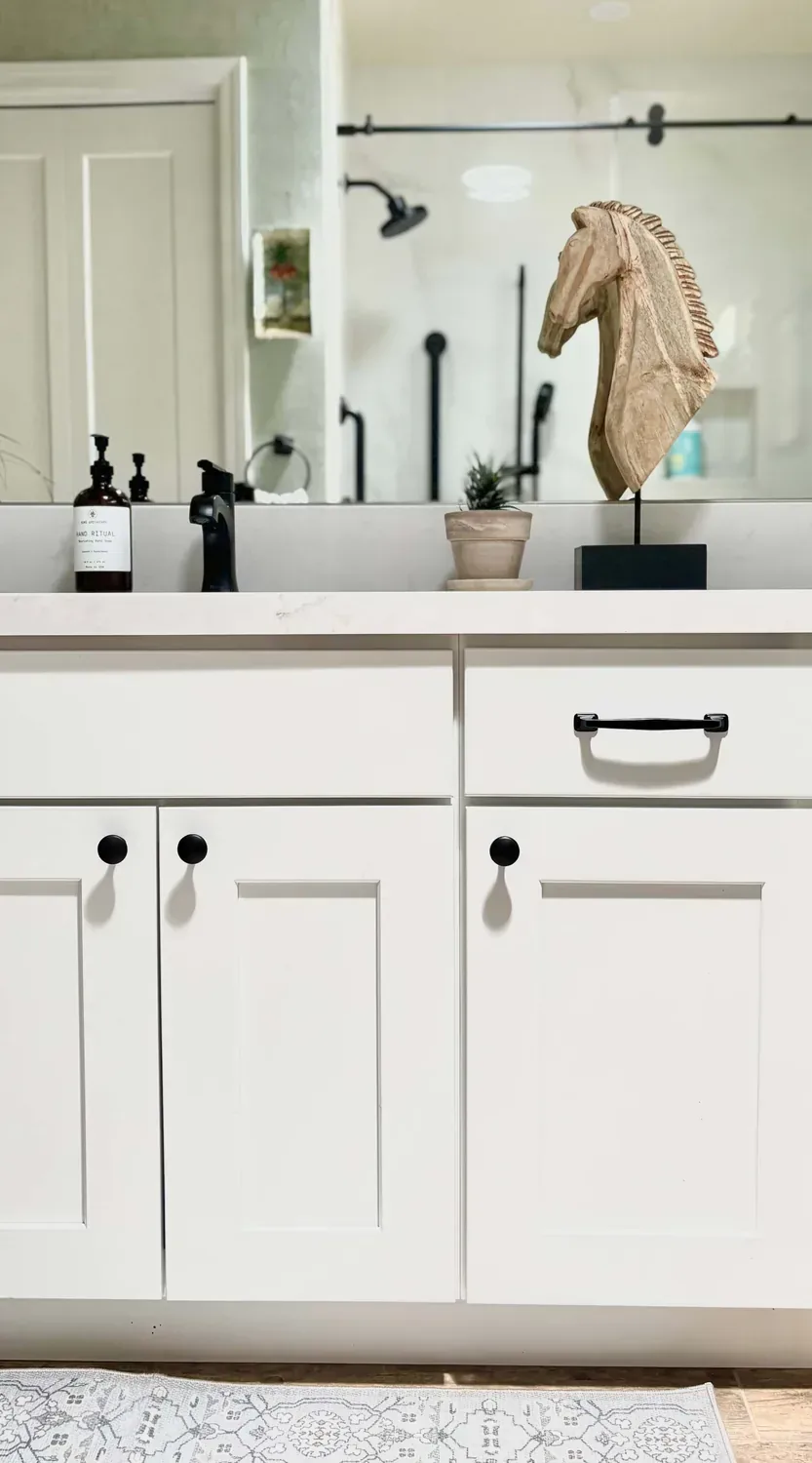 A modern bathroom vanity with white cabinets, black hardware, a black faucet, a wooden horse head sculpture, a small