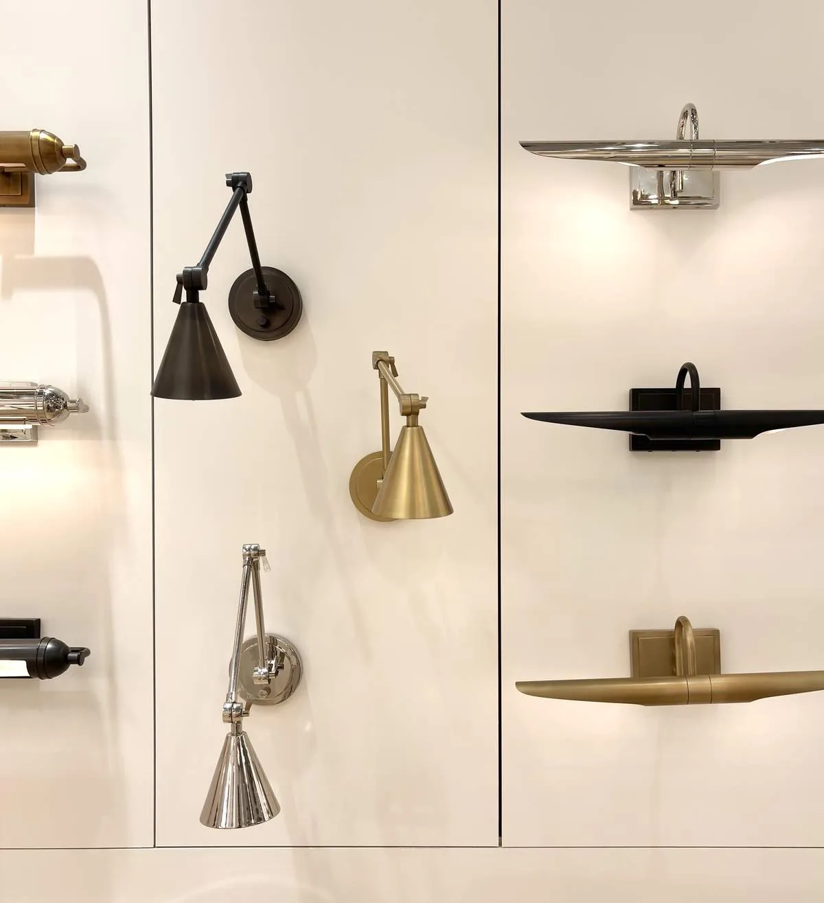 A display of various modern wall-mounted light fixtures in different finishes on a white wall