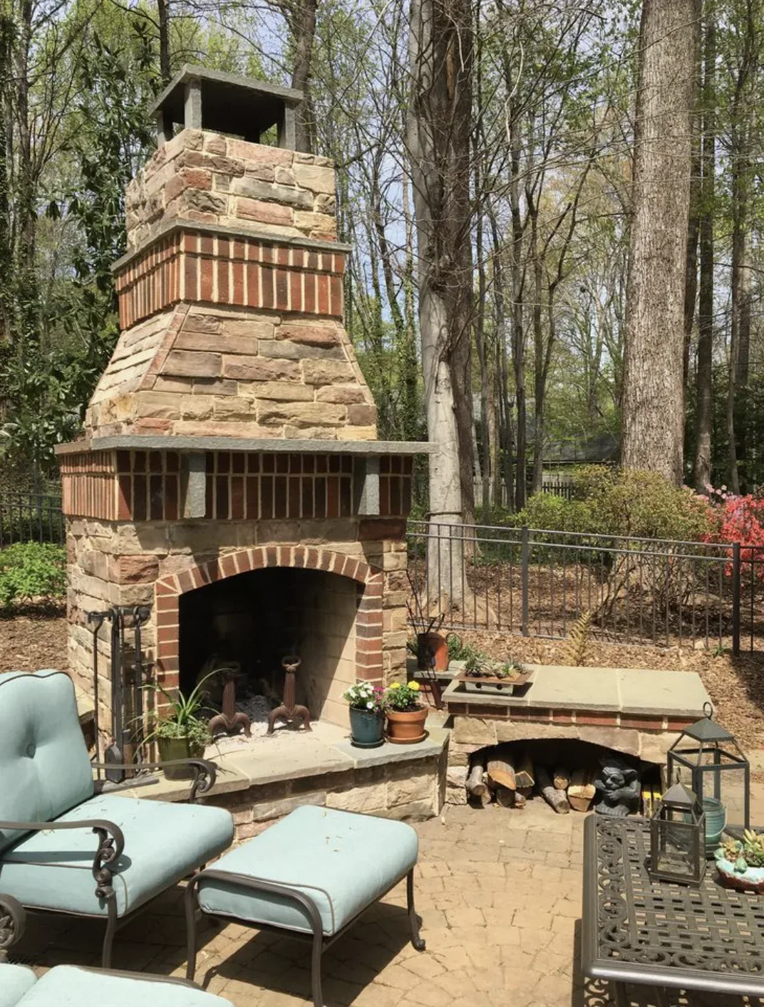 Outdoor patio area with a stone and brick fireplace, seating, and decorative plants