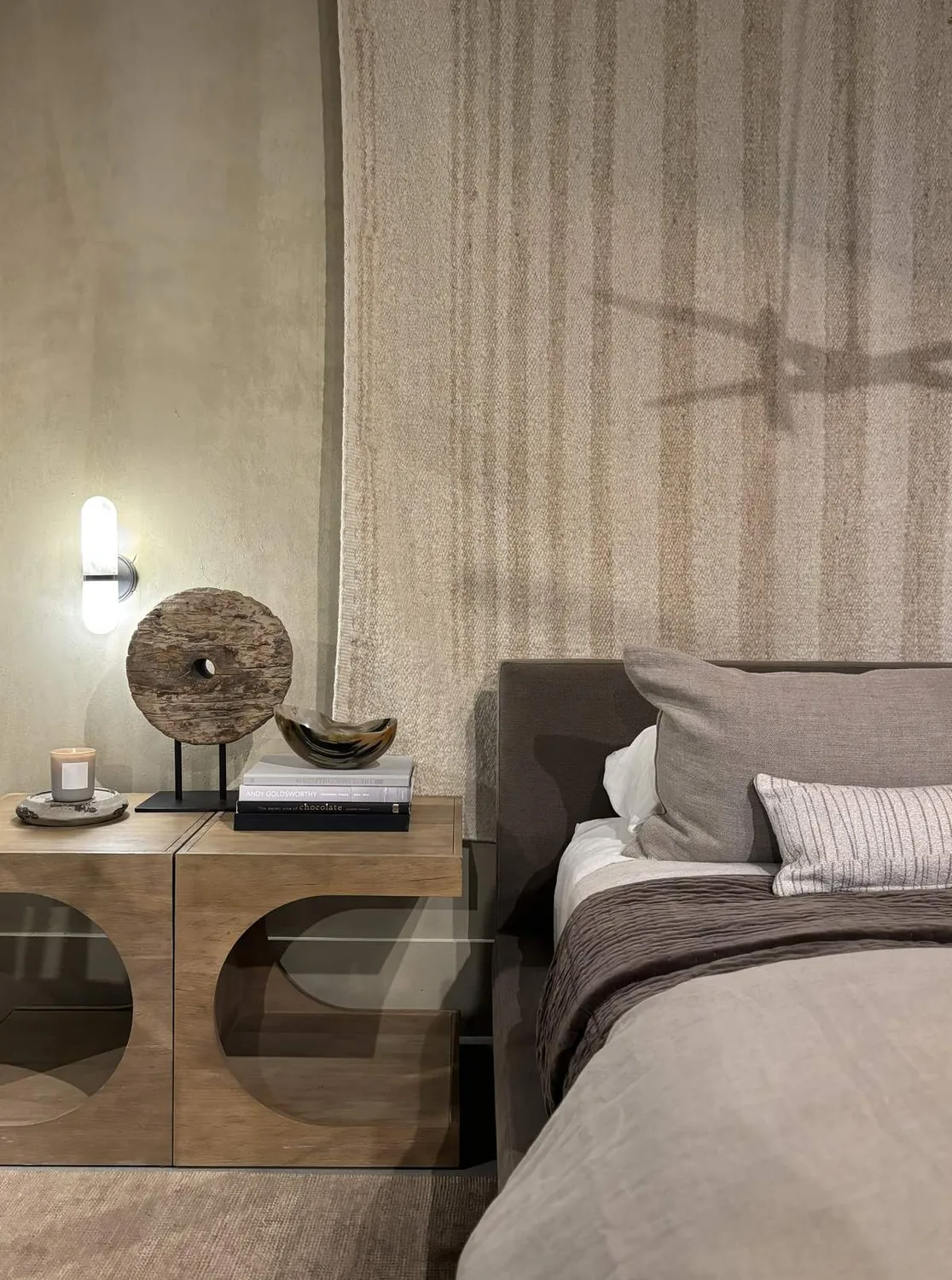 A modern bedroom corner with a wooden nightstand, decorative objects, and neutral-toned bedding