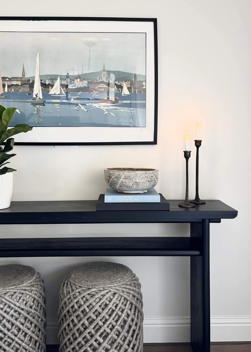 A minimalist dining room with a round black table, four chairs, a black geometric chandelier, and a large window