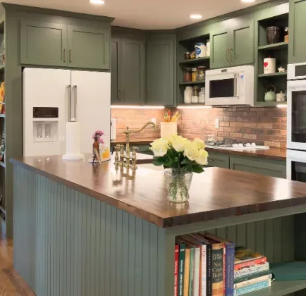 A kitchen with green cabinetry, a wooden countertop island, white appliances, and a brick backsplash