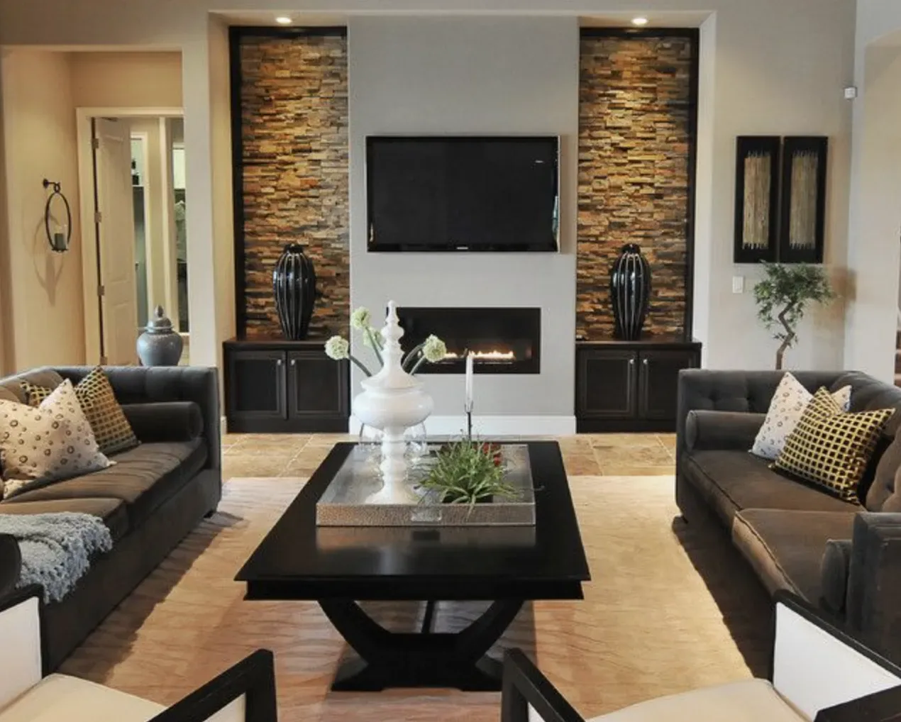 A modern living room with two dark sofas facing a black coffee table, a wall-mounted TV above a fireplace