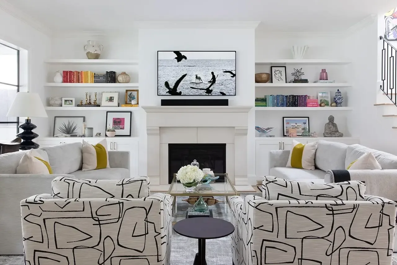 A modern living room corner featuring a white tiled fireplace with a woven basket, a small side table with books