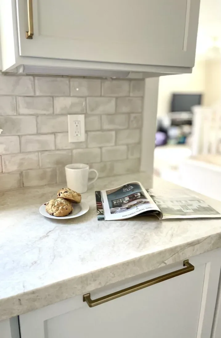 A kitchen countertop with a plate of cookies, a white mug, and an open magazine, featuring a light-colored marble